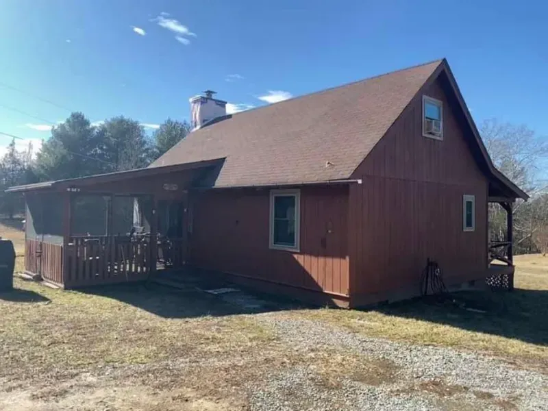 Brown wooden house with porch and brown roof under a blue sky.