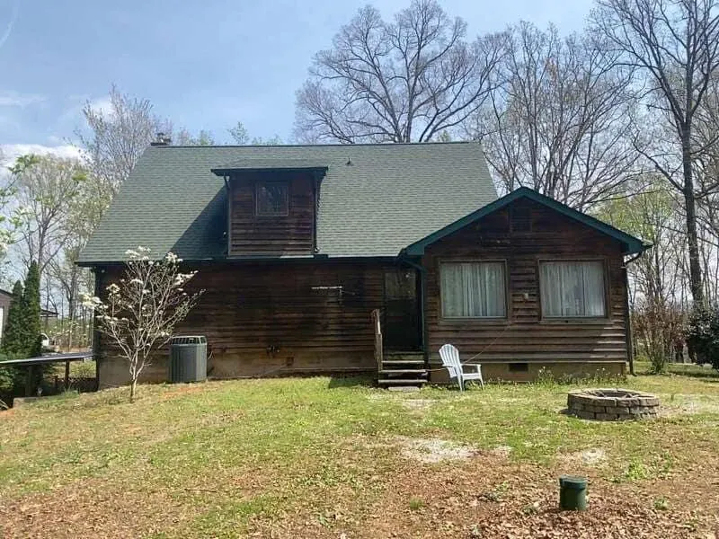 Log cabin with green roof and dormer window, set in a grassy yard, under a blue sky.