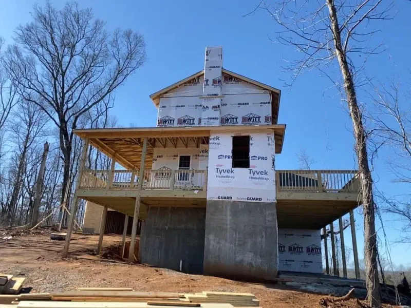 House under construction with a concrete foundation, wooden deck, and chimney; set against a clear blue sky.