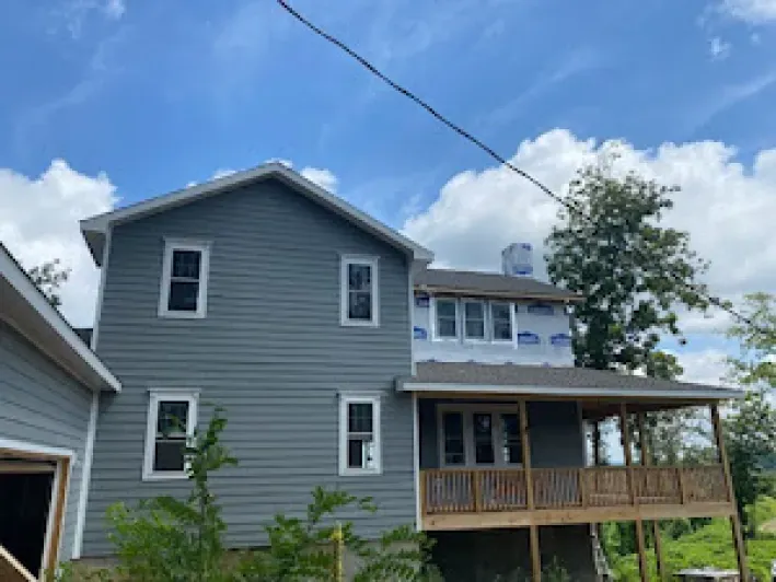 Two-story house with gray siding, a porch, and a detached garage, under a blue sky.