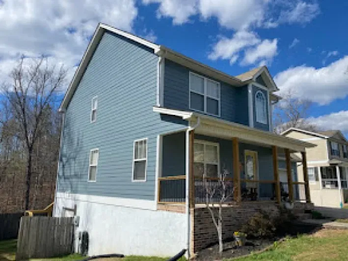 Blue two-story house with porch and white foundation against a partly cloudy sky.