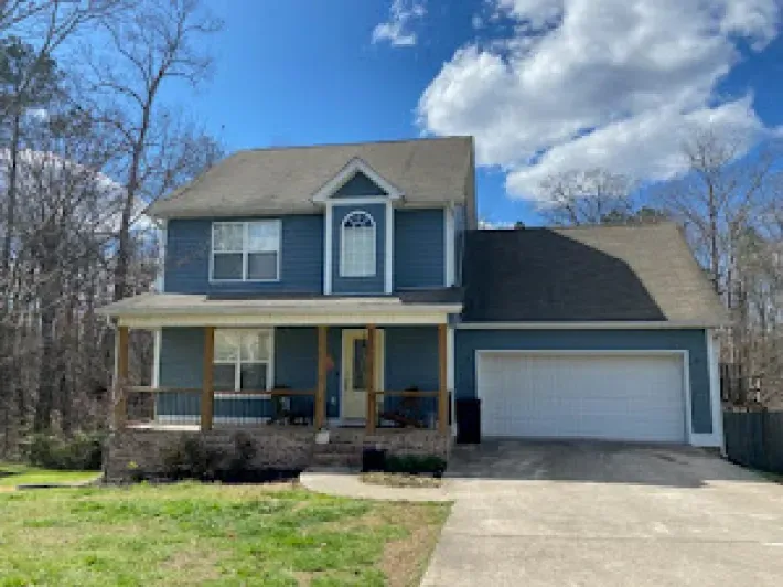 Two-story blue house with a covered porch and attached garage on a sunny day.