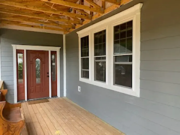 Gray house exterior with red door, white-trimmed windows, and wooden porch.