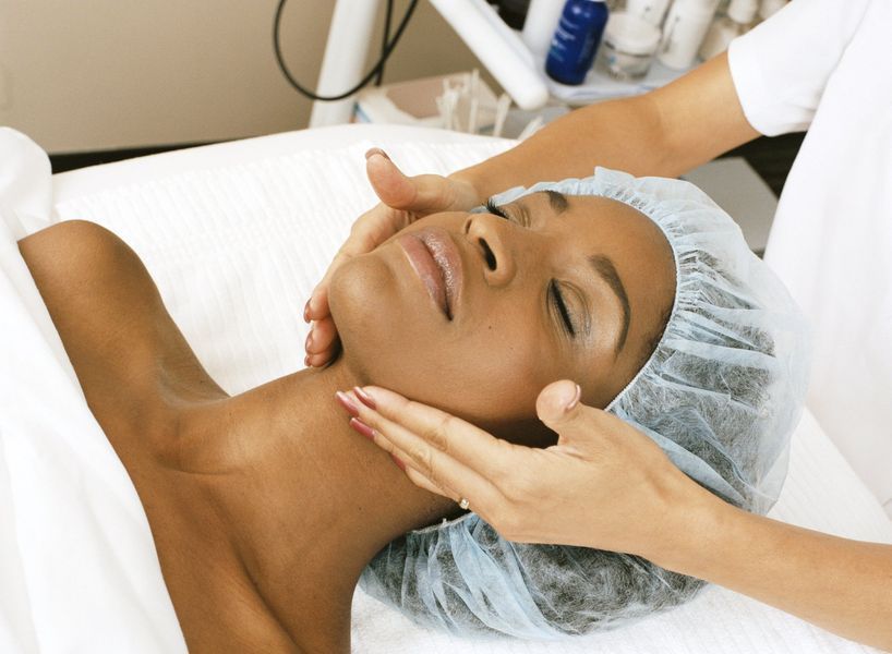 A professional aesthetician gives a facial massage to a client lying on a treatment table.