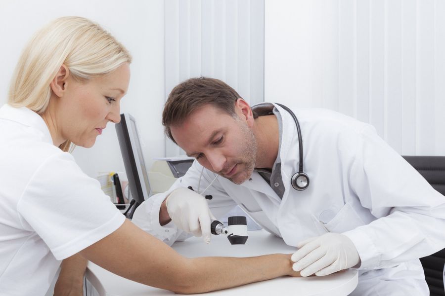 A doctor uses a dermatoscope to examine a patient’s arm in a medical office.