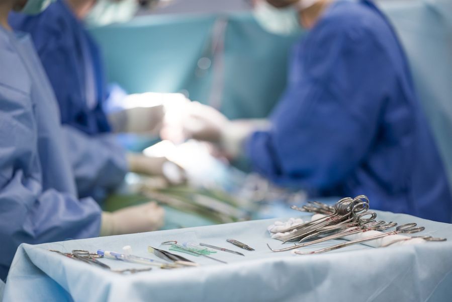 Surgical instruments lay on a sterile blue drape in the foreground, with medical staff in blue scrubs working in the back.