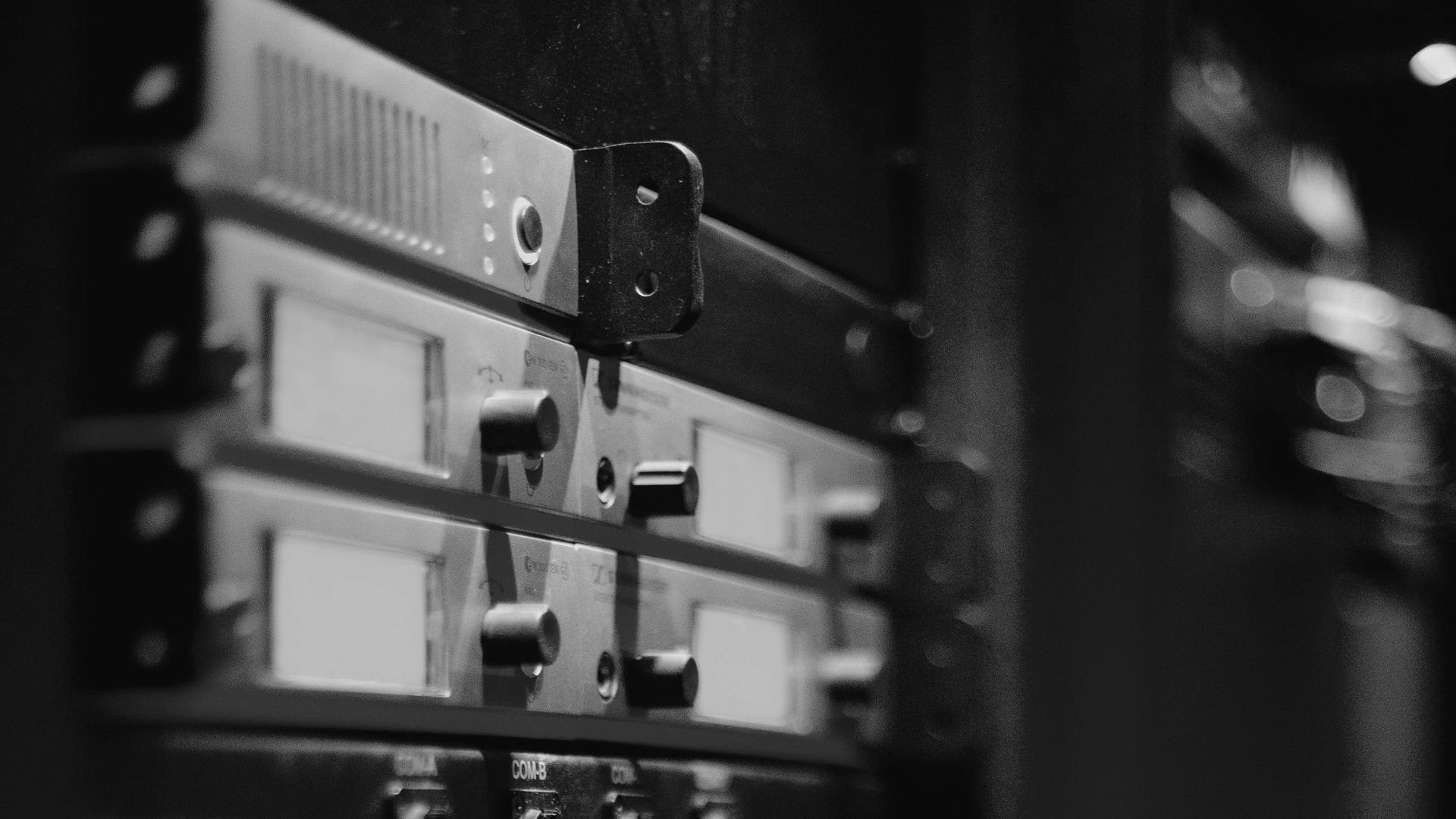 Black and white image of electronic equipment rack with knobs and display screens.