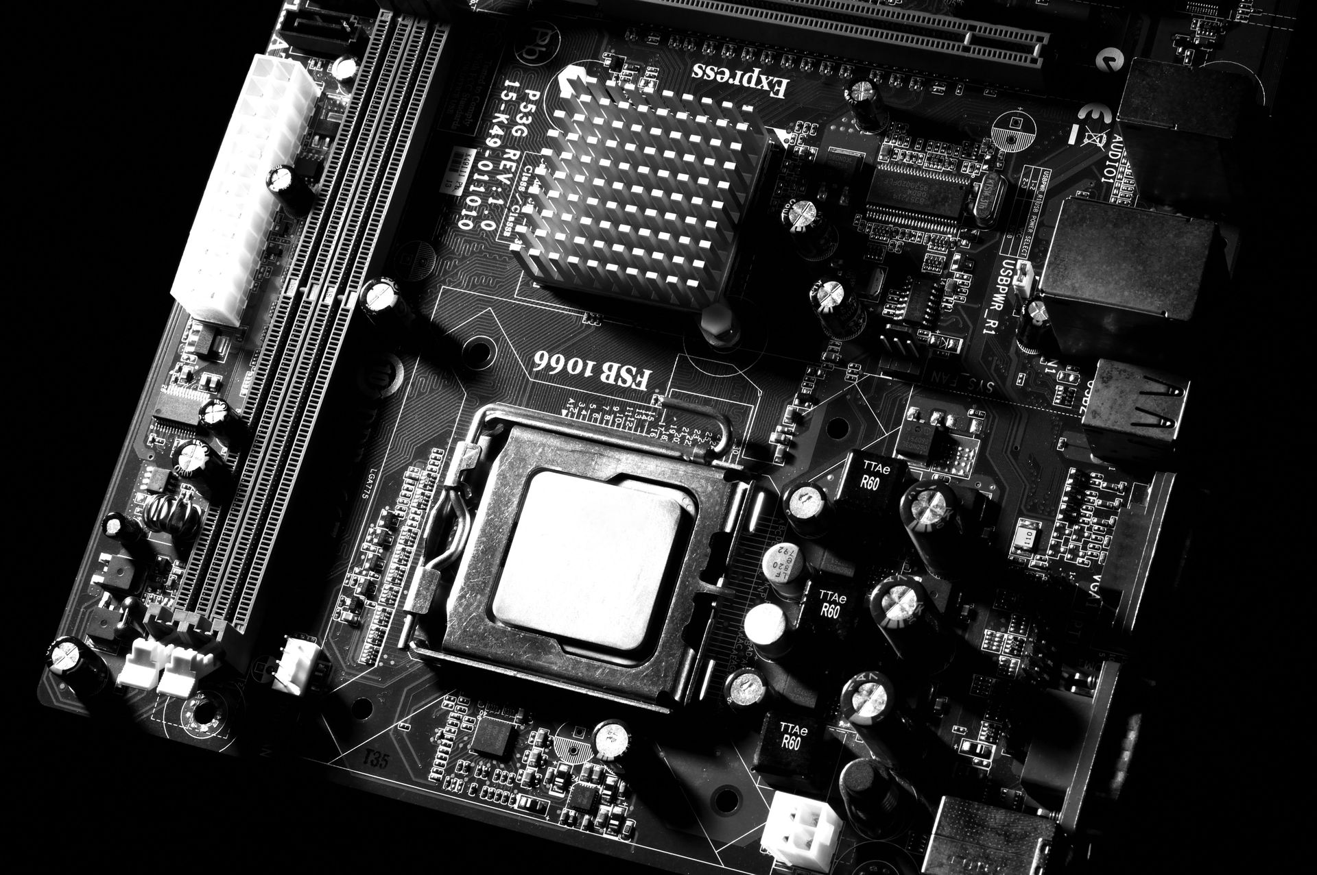 Black and white close-up of a computer motherboard, showing a central processing unit (CPU) and surrounding components.