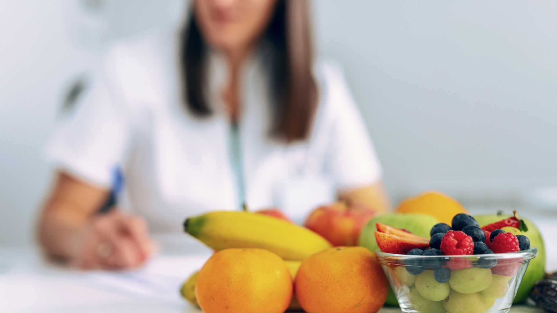 A woman is sitting at a table with a bowl of fruit.