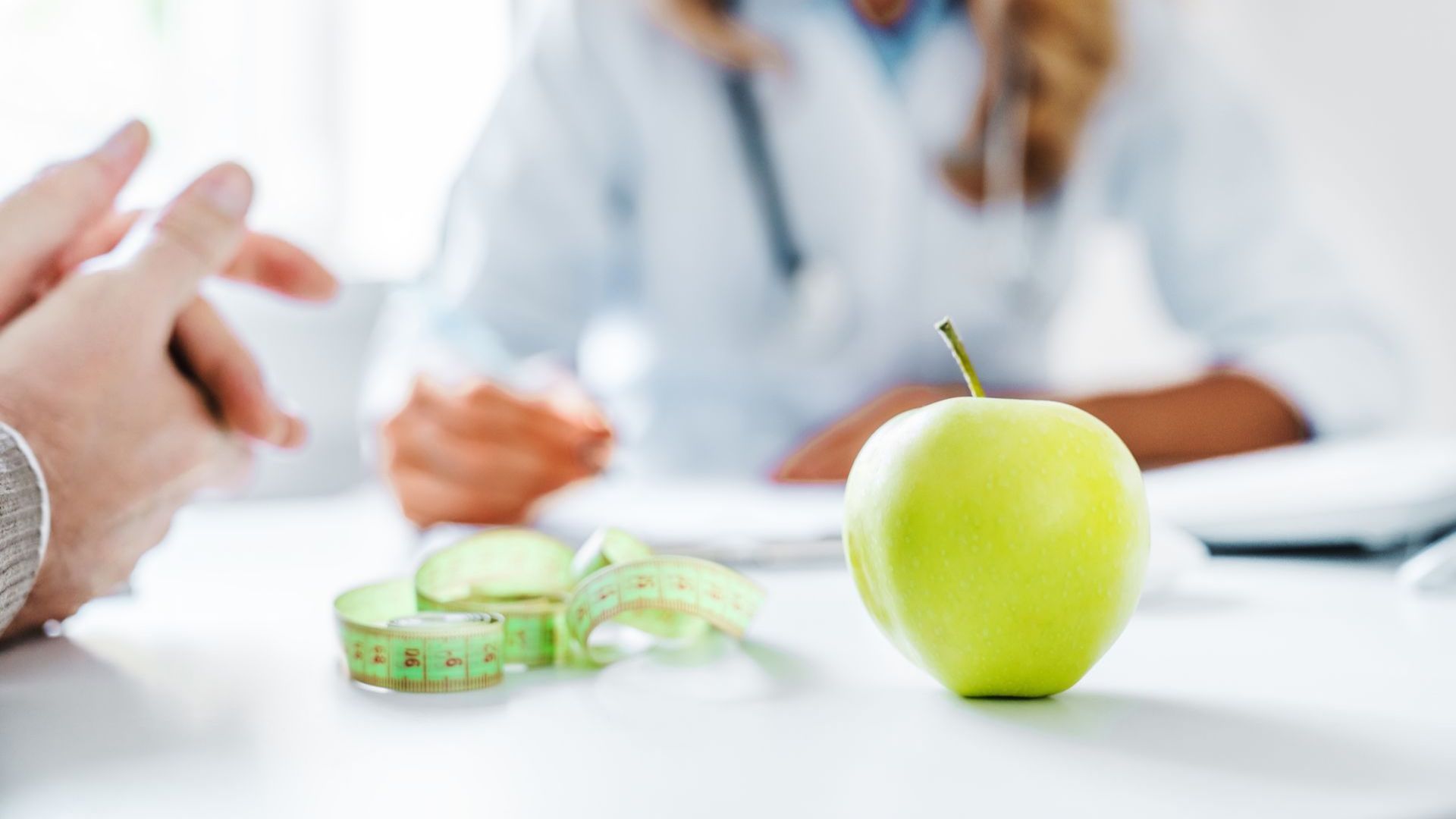 A green apple is sitting on a table next to a measuring tape.