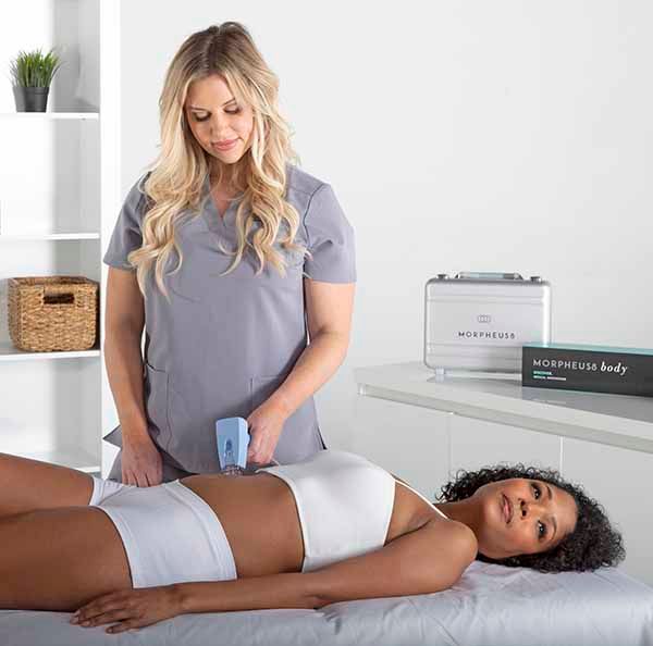 A woman is standing next to a woman laying on a bed.