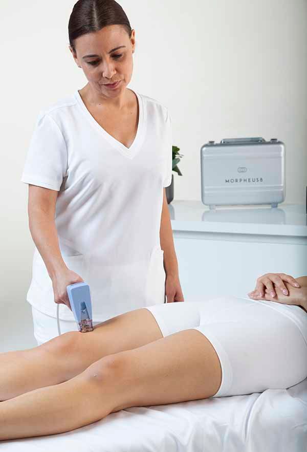 A woman in a white shirt is standing next to a woman laying on a bed.