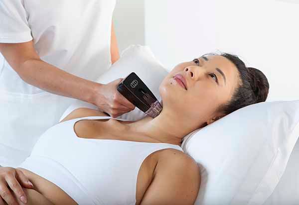 A woman is laying on a bed getting a treatment on her neck.