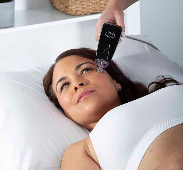 A woman is laying on a bed getting a treatment on her face.
