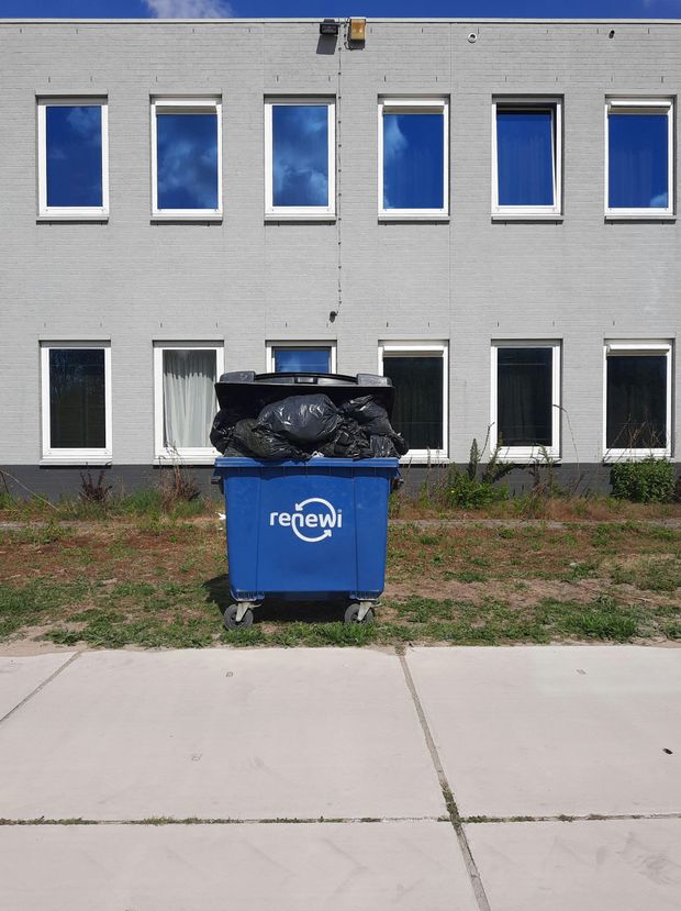 A blue recycling bin sits in front of a building