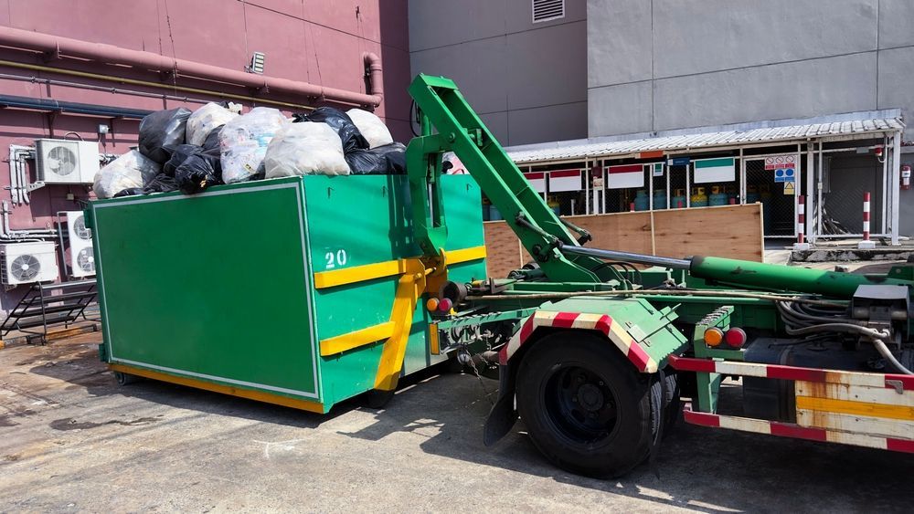A green dumpster is being pulled by a garbage truck.