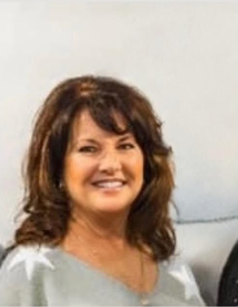 Woman with brown hair smiling, wearing a light sweater, looking at the camera.