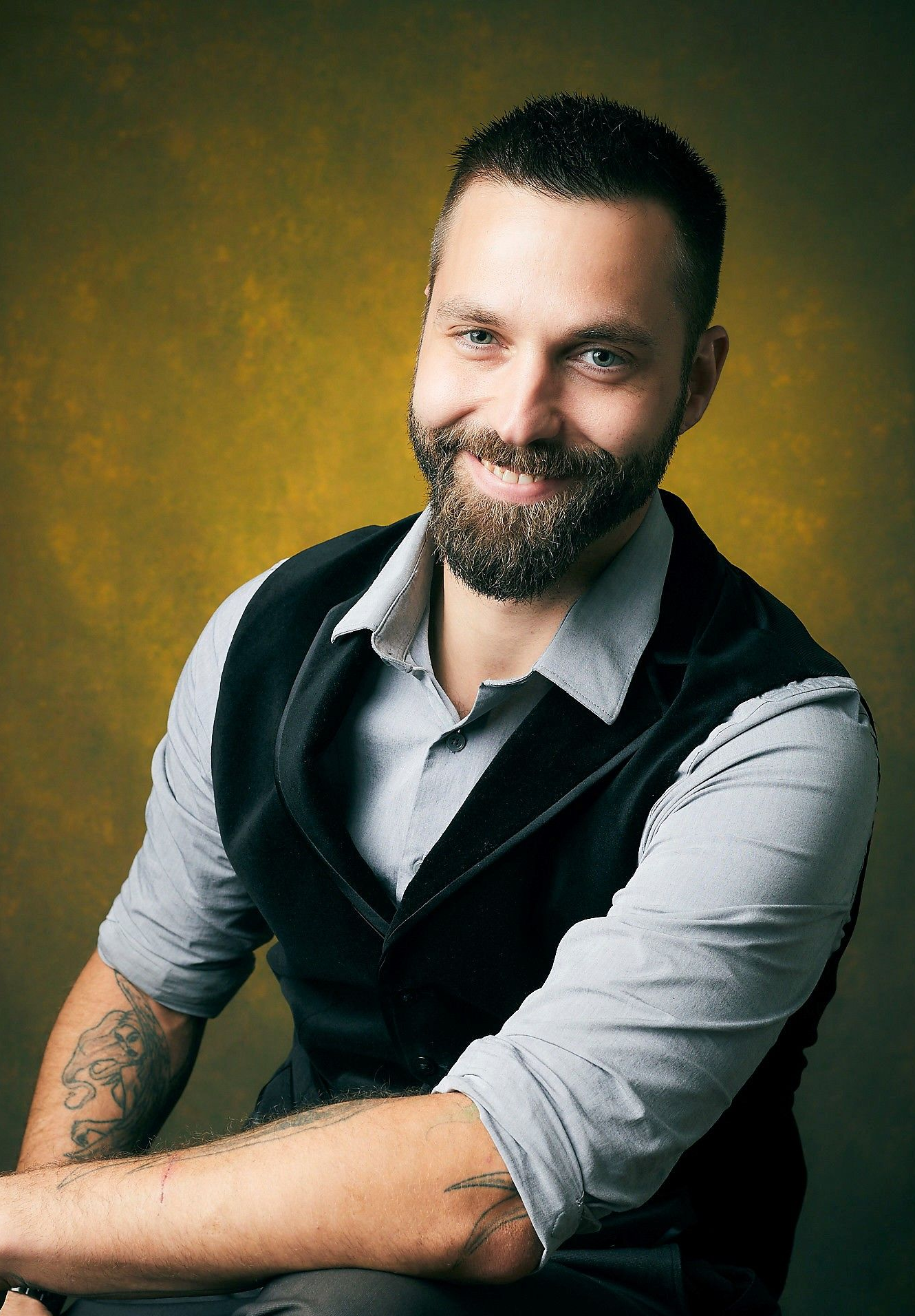 Woman wearing glasses and a plaid jacket smiles, with a background of green foliage.