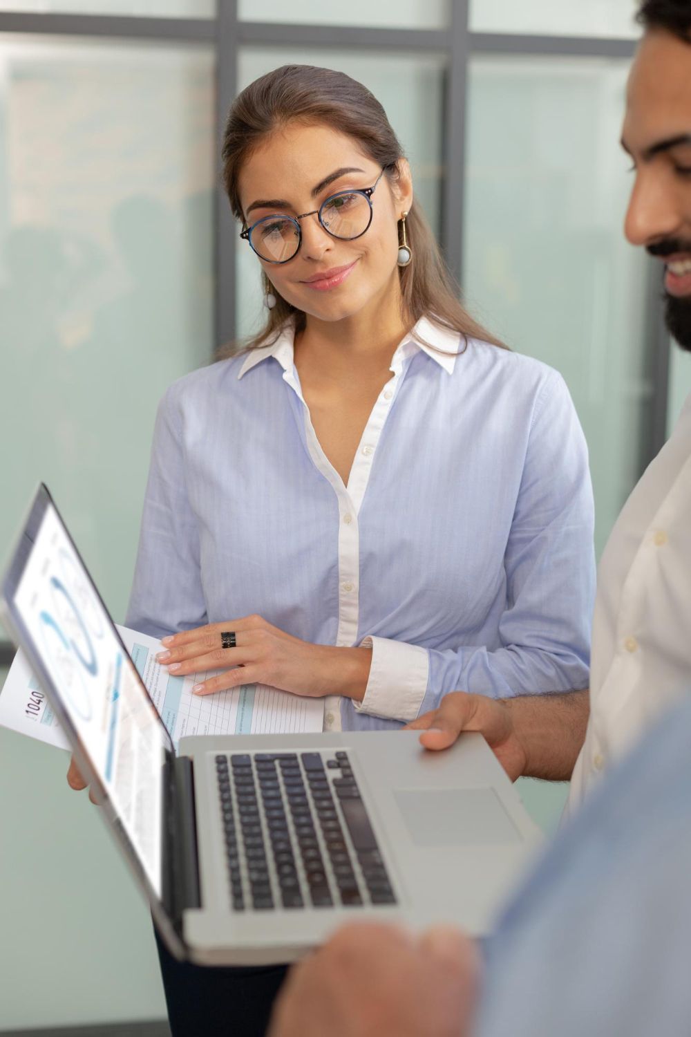 A group of young people are standing around a table looking at a laptop.