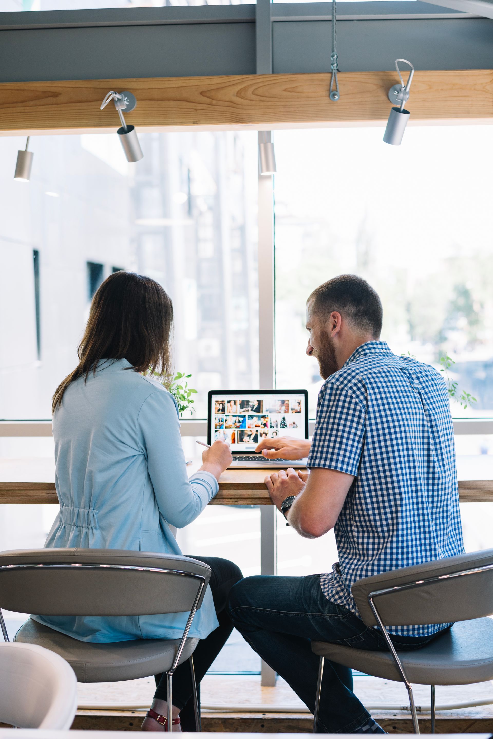 A man and a woman are sitting at a table looking at a laptop.