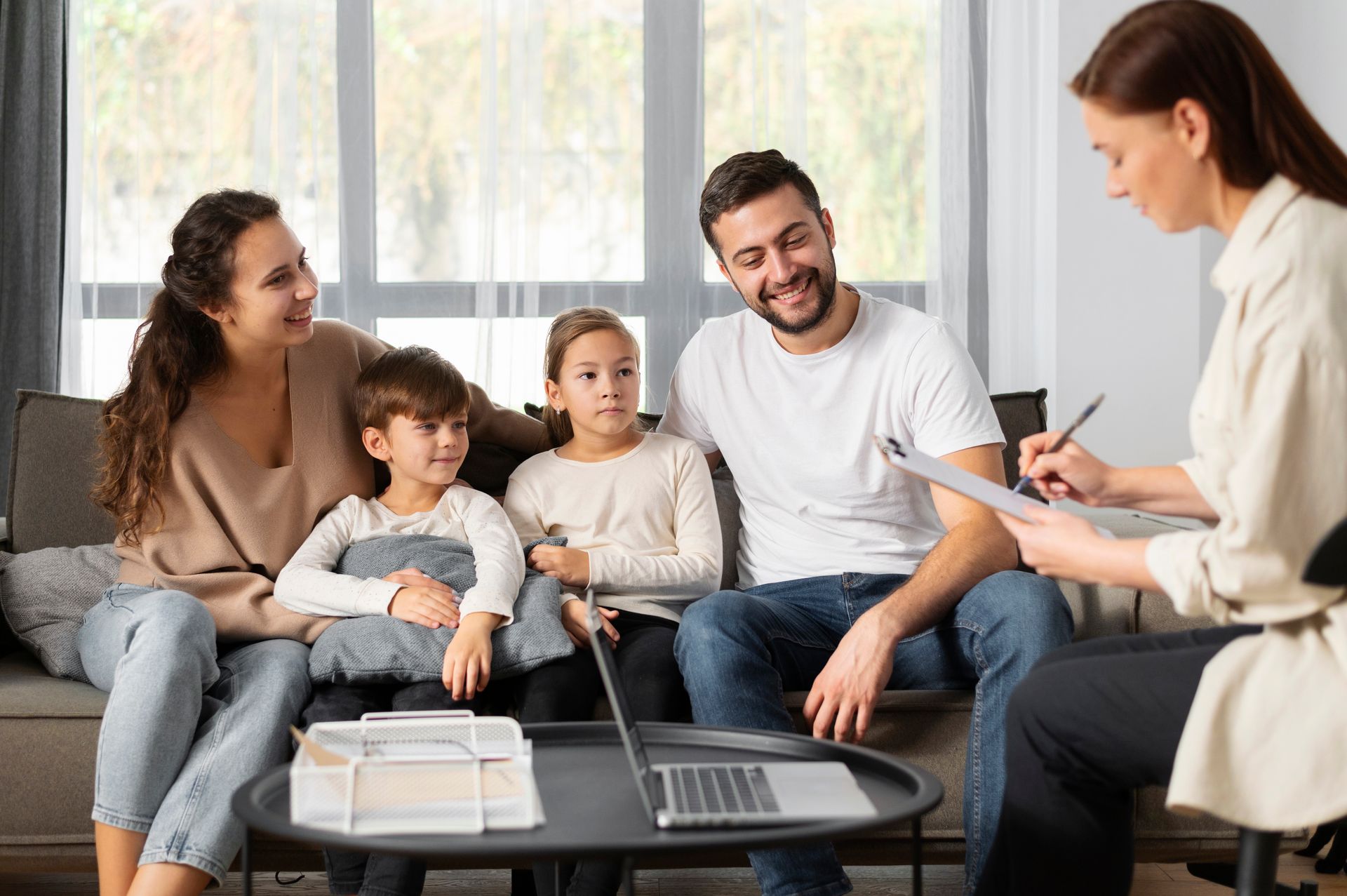 A family is sitting on a couch talking to a woman.