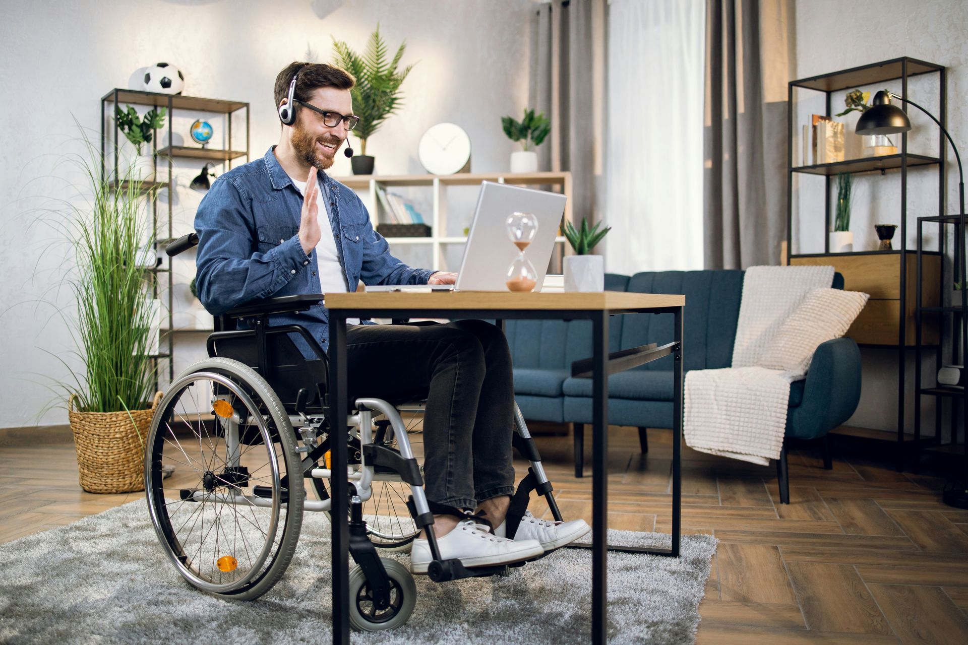 A man in a wheelchair is sitting at a desk using a laptop computer.