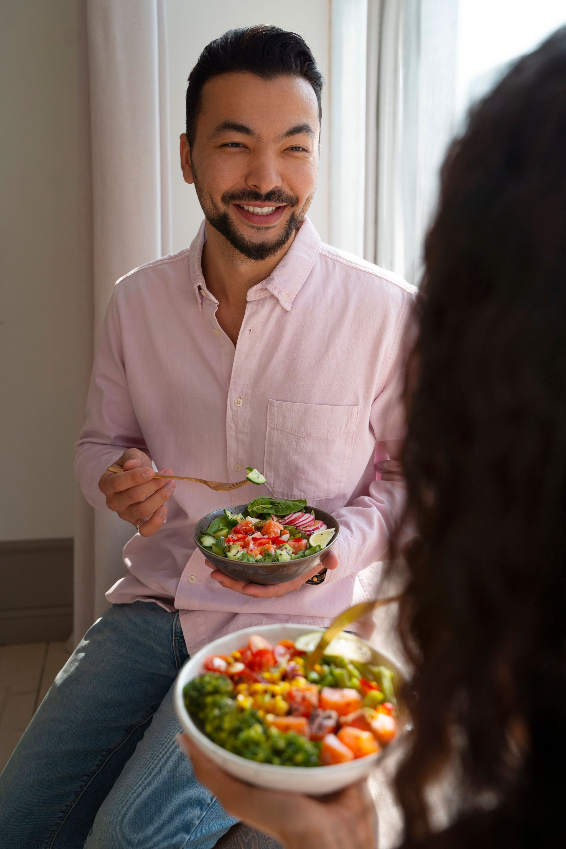 A man is sitting next to a woman holding a bowl of salad.