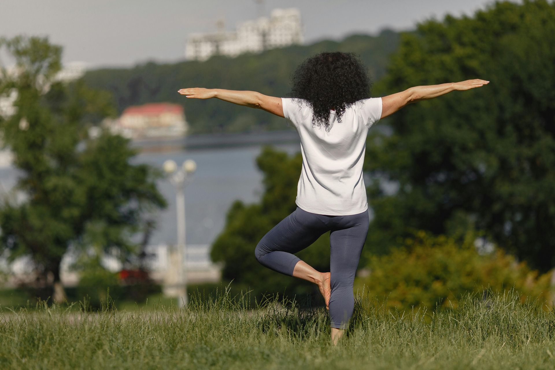 A woman is practicing yoga in a park with her arms outstretched.