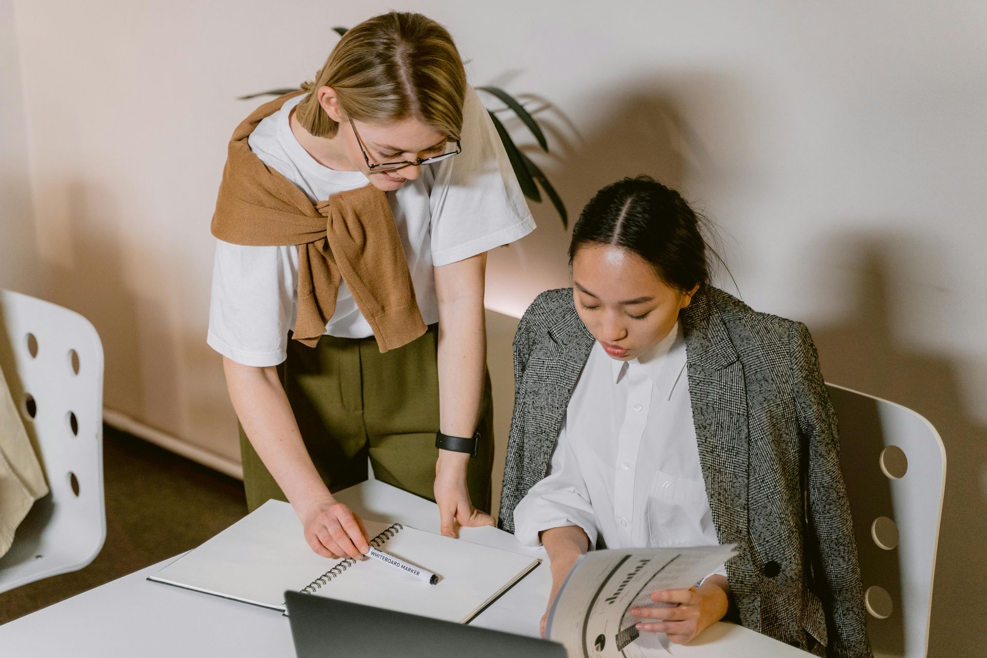 Two women are sitting at a table looking at a laptop computer.