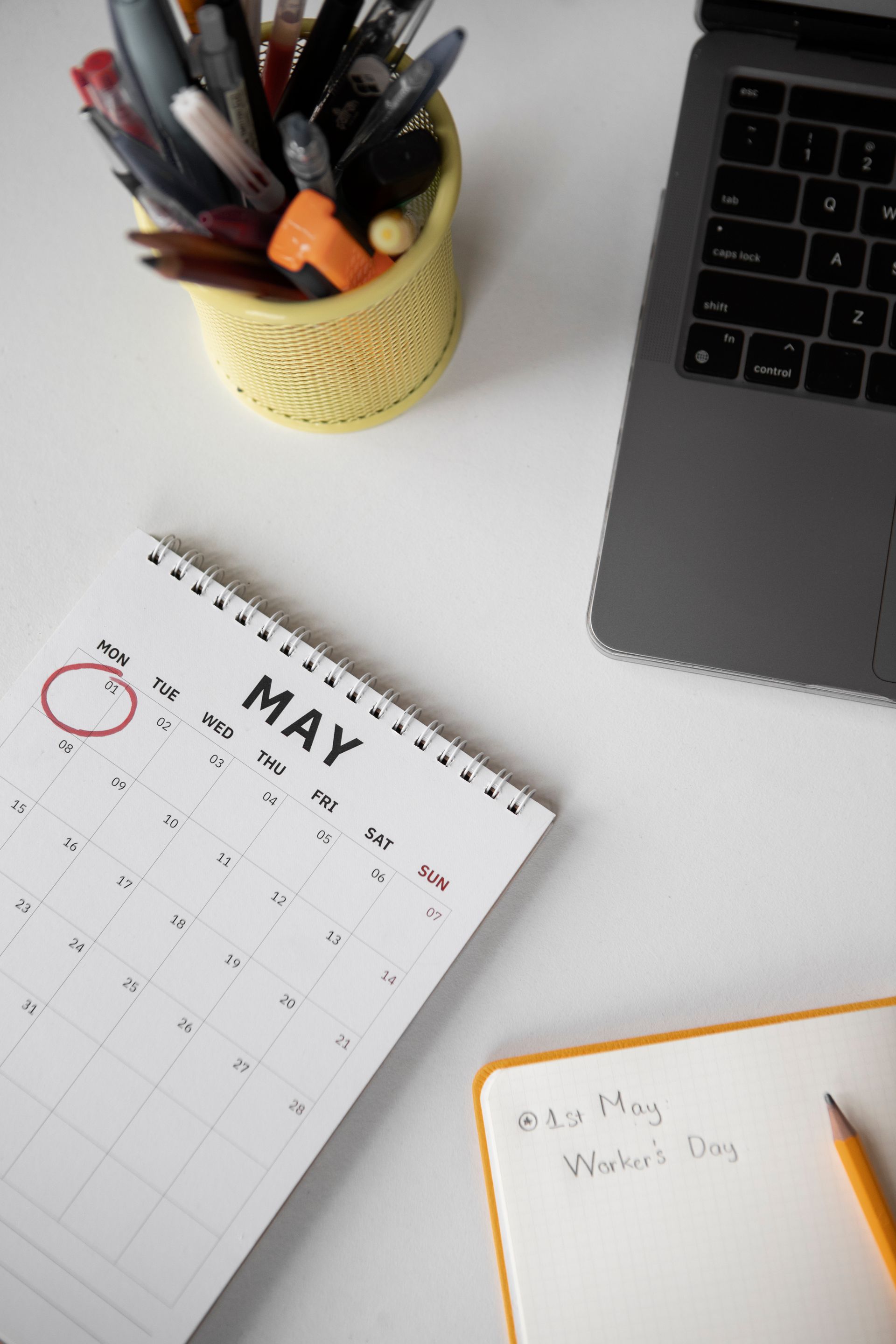A calendar is sitting on a desk next to a laptop and a pen holder.