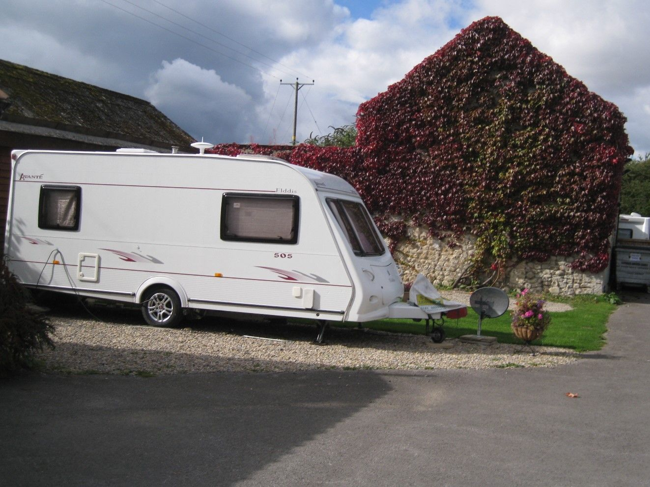 White caravan parked near stone building with red foliage.