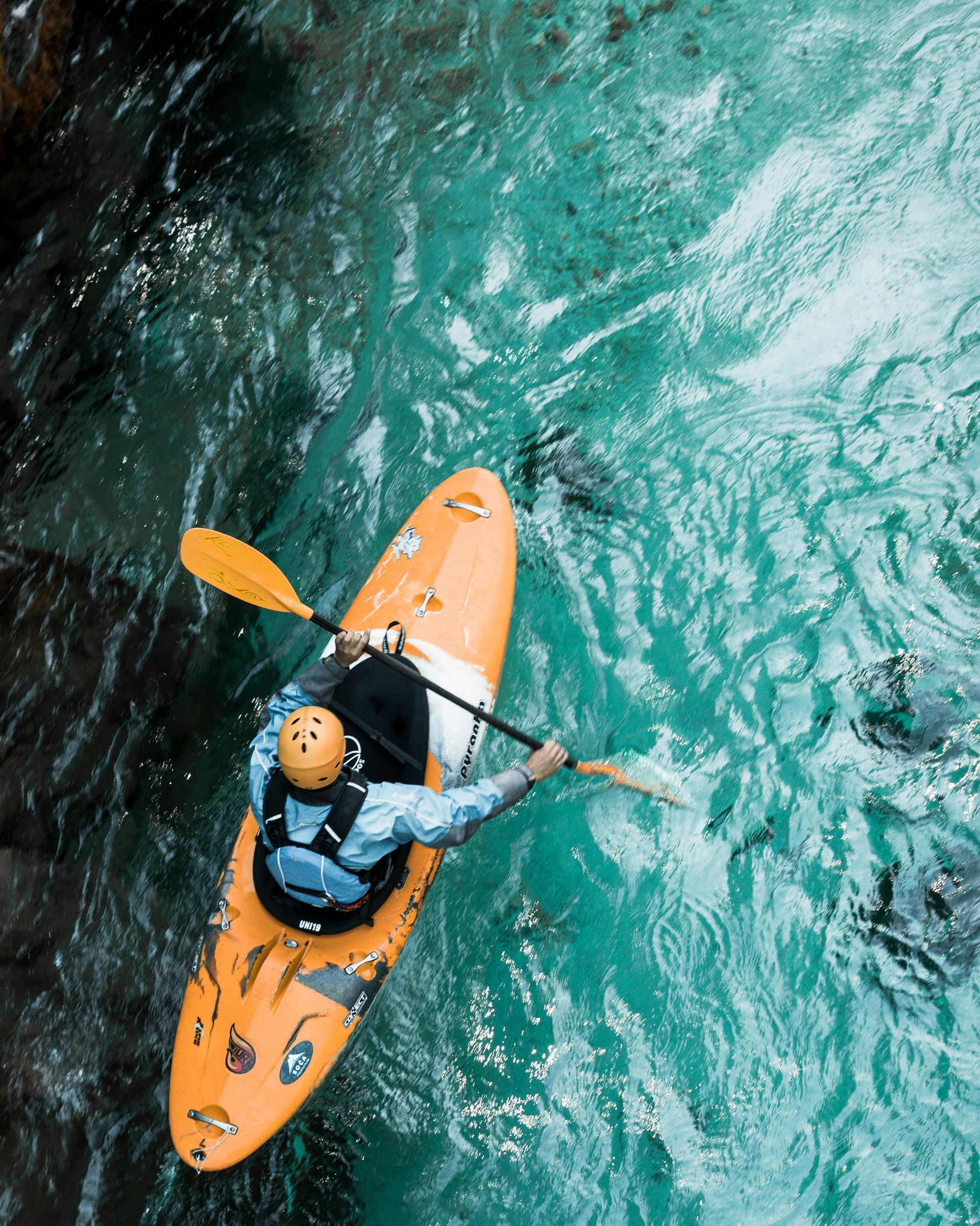 Kayaker paddling through turquoise water in an orange kayak, overhead view.