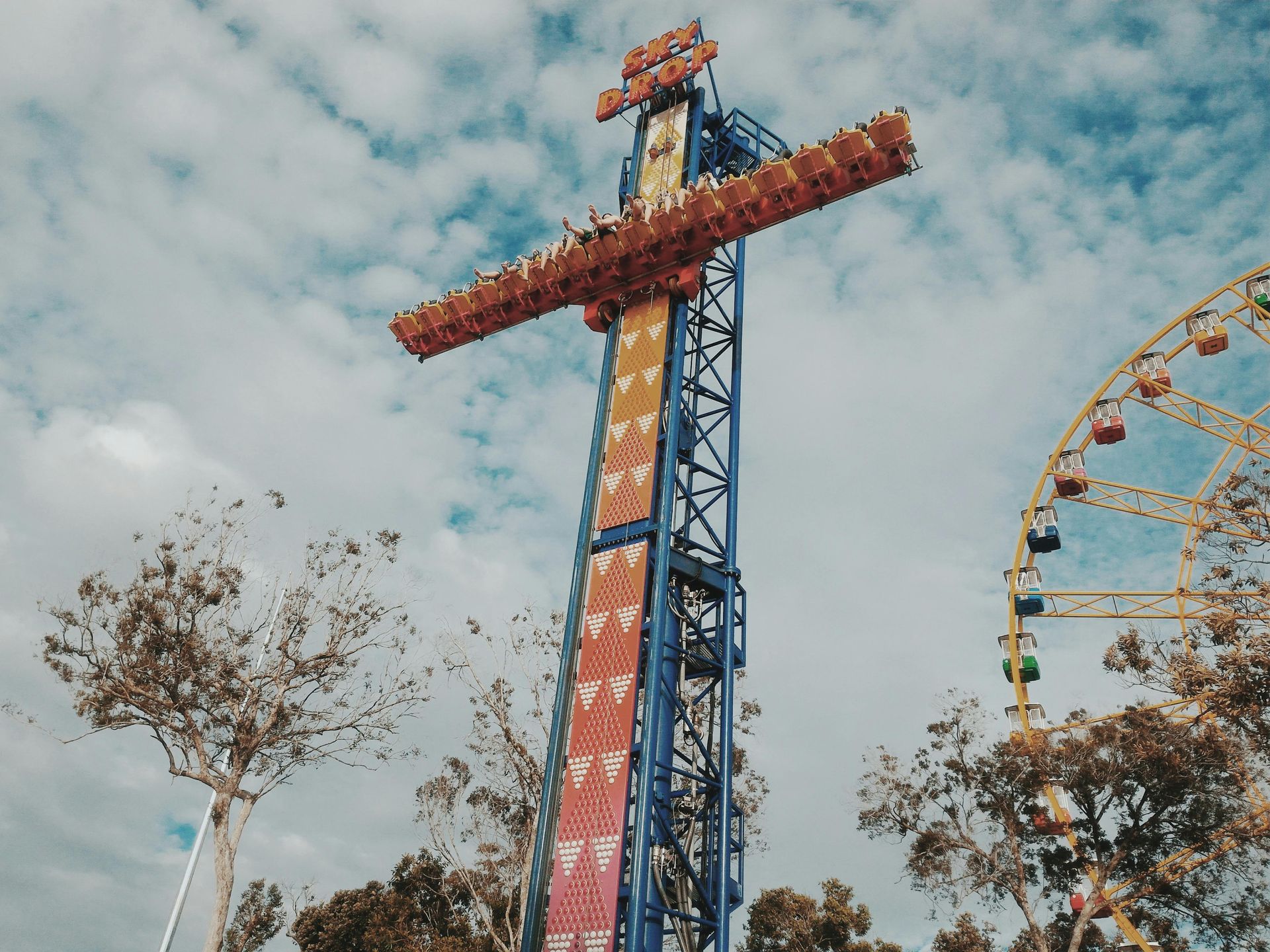 Amusement park ride with seats on a tall tower, a Ferris wheel, and cloudy sky.