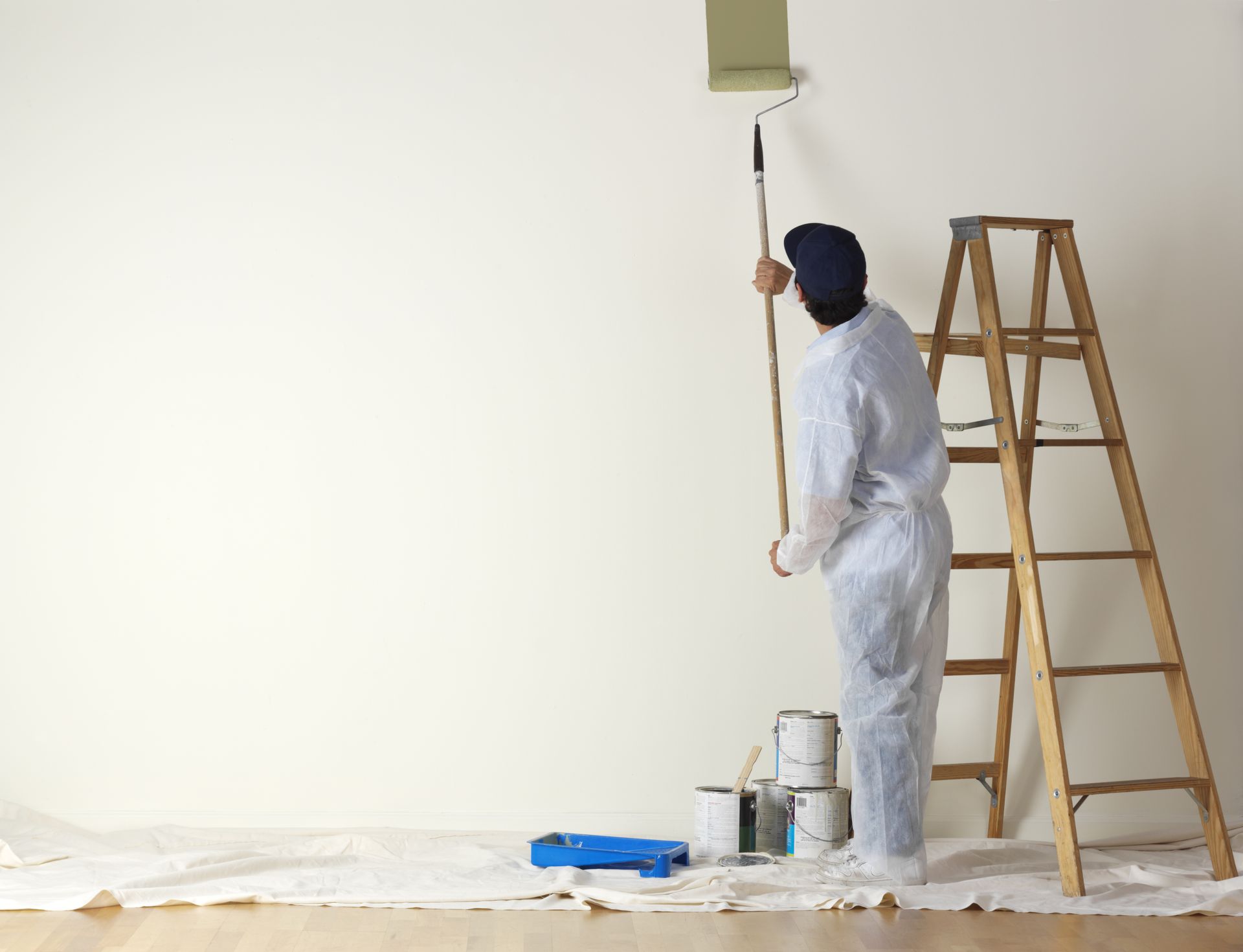A man is standing on a ladder painting a wall.