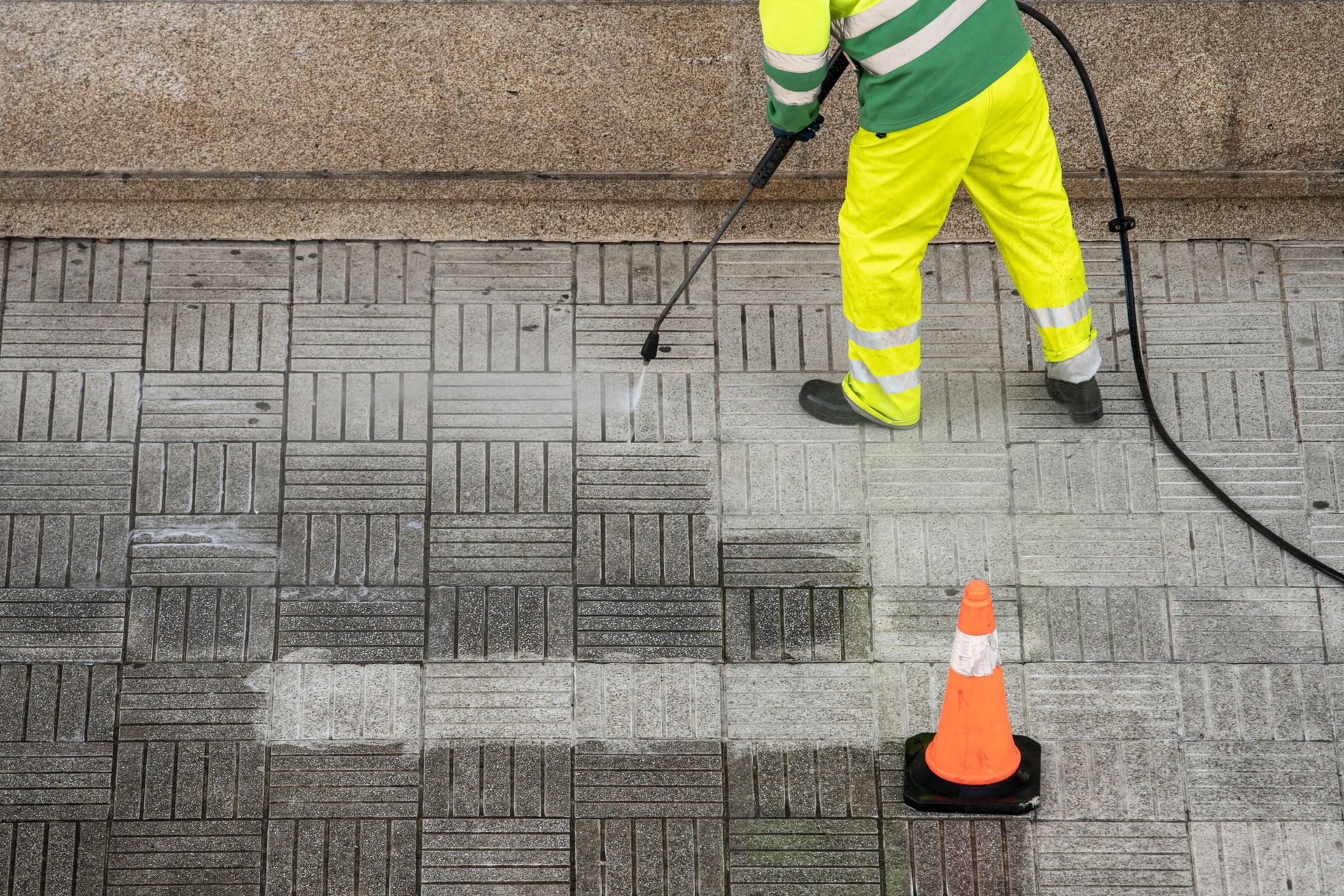 A man is cleaning the sidewalk with a high pressure washer.