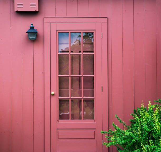 A pink door with a glass window is on a red building.