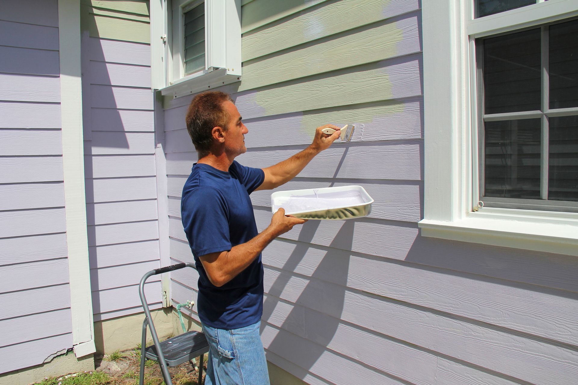 A man is painting the side of a house with a roller.