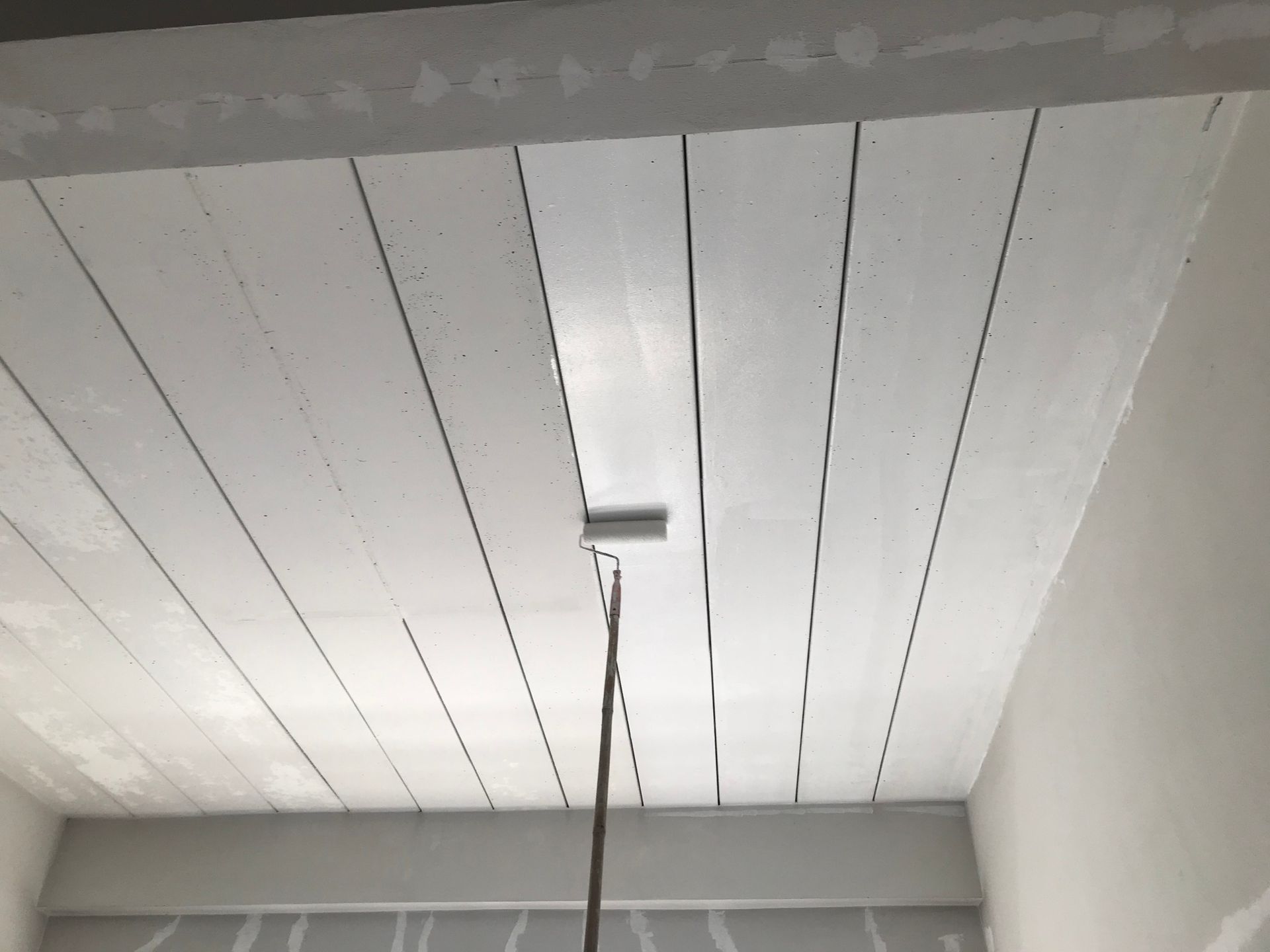 A person is painting a white ceiling with a roller.