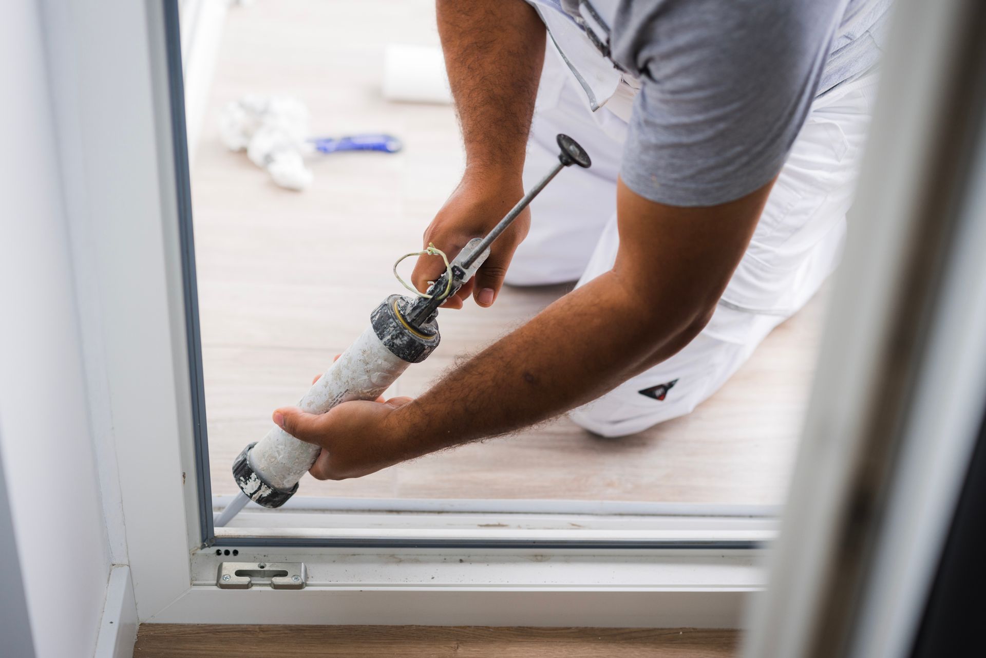 A man is applying sealant to a window frame.