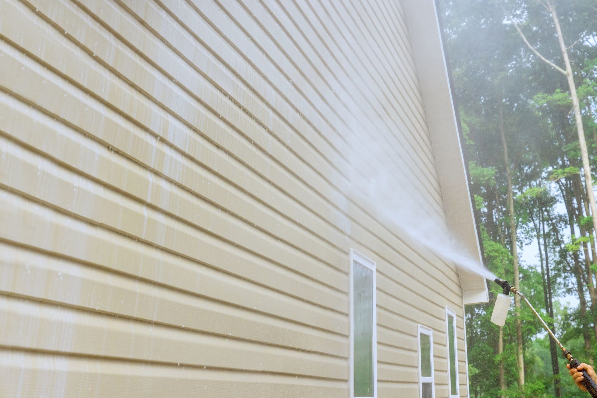 A man is using a high pressure washer to clean the side of a house.