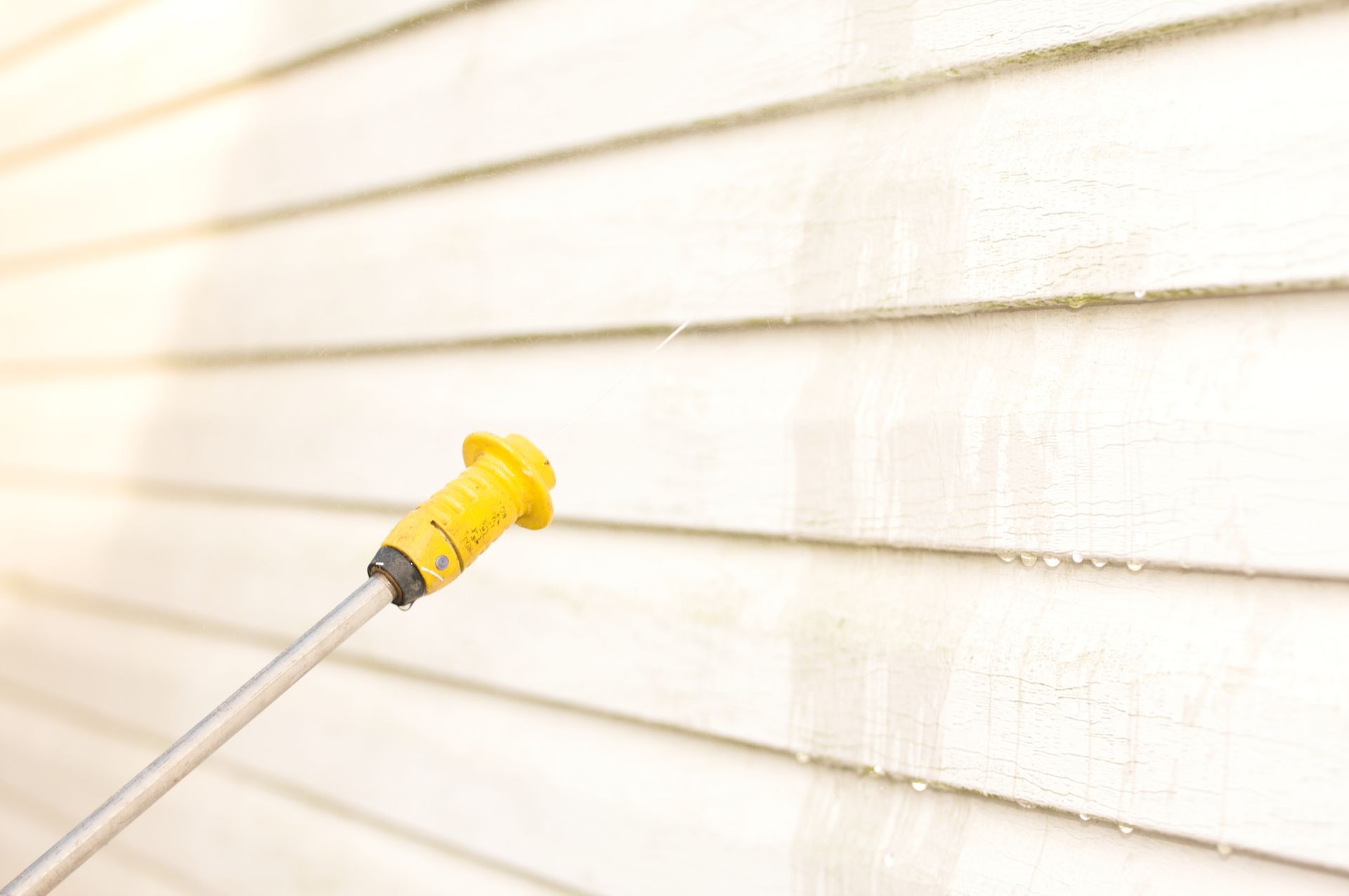 A person is using a high pressure washer to clean the side of a house.