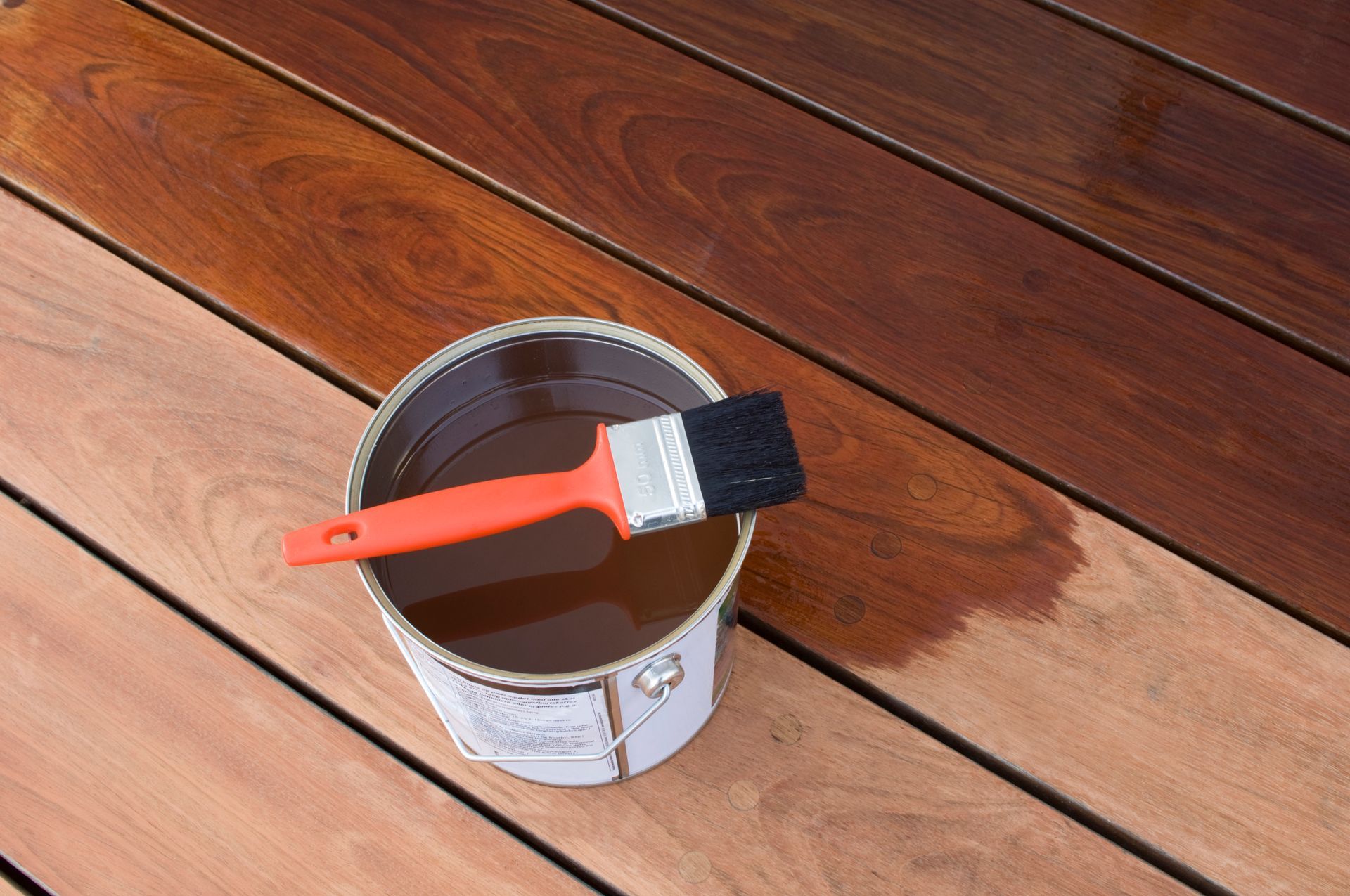 A can of paint and a brush on a wooden deck.
