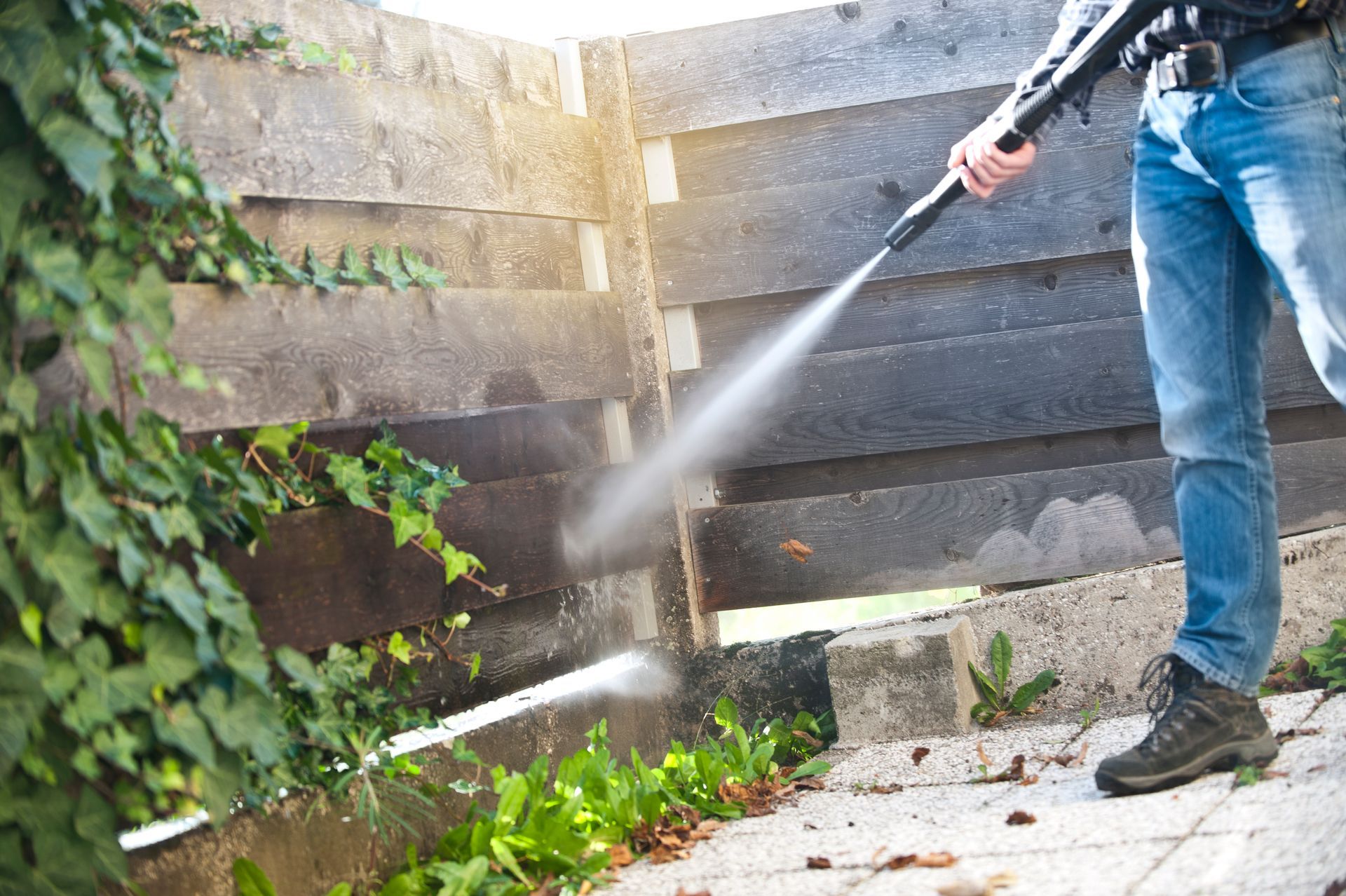 A man is using a high pressure washer to clean a fence.