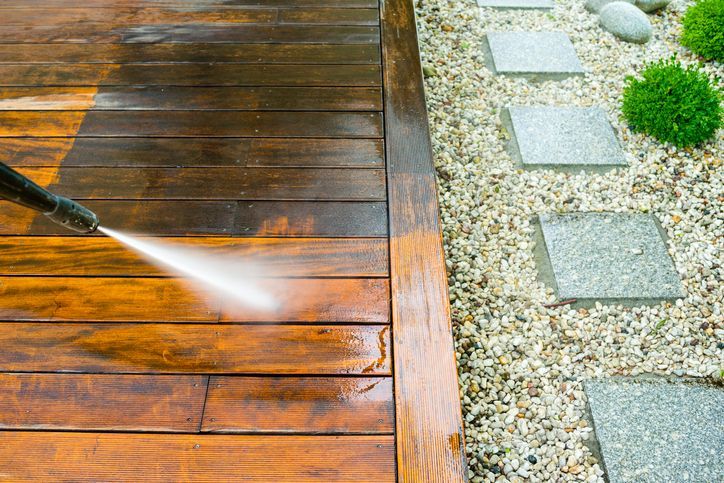 A person is cleaning a wooden deck with a high pressure washer.