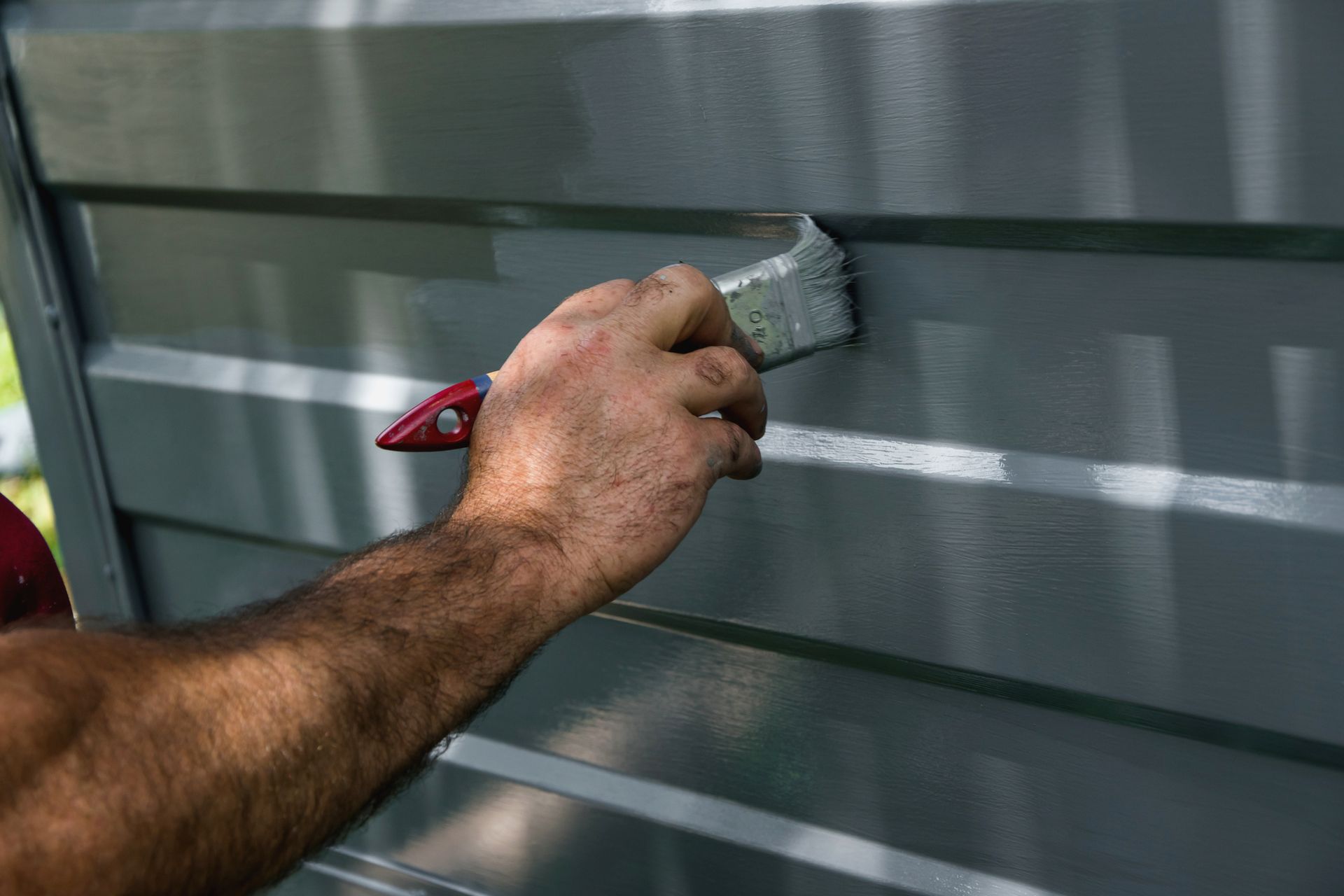 A man is painting a metal fence with a brush.