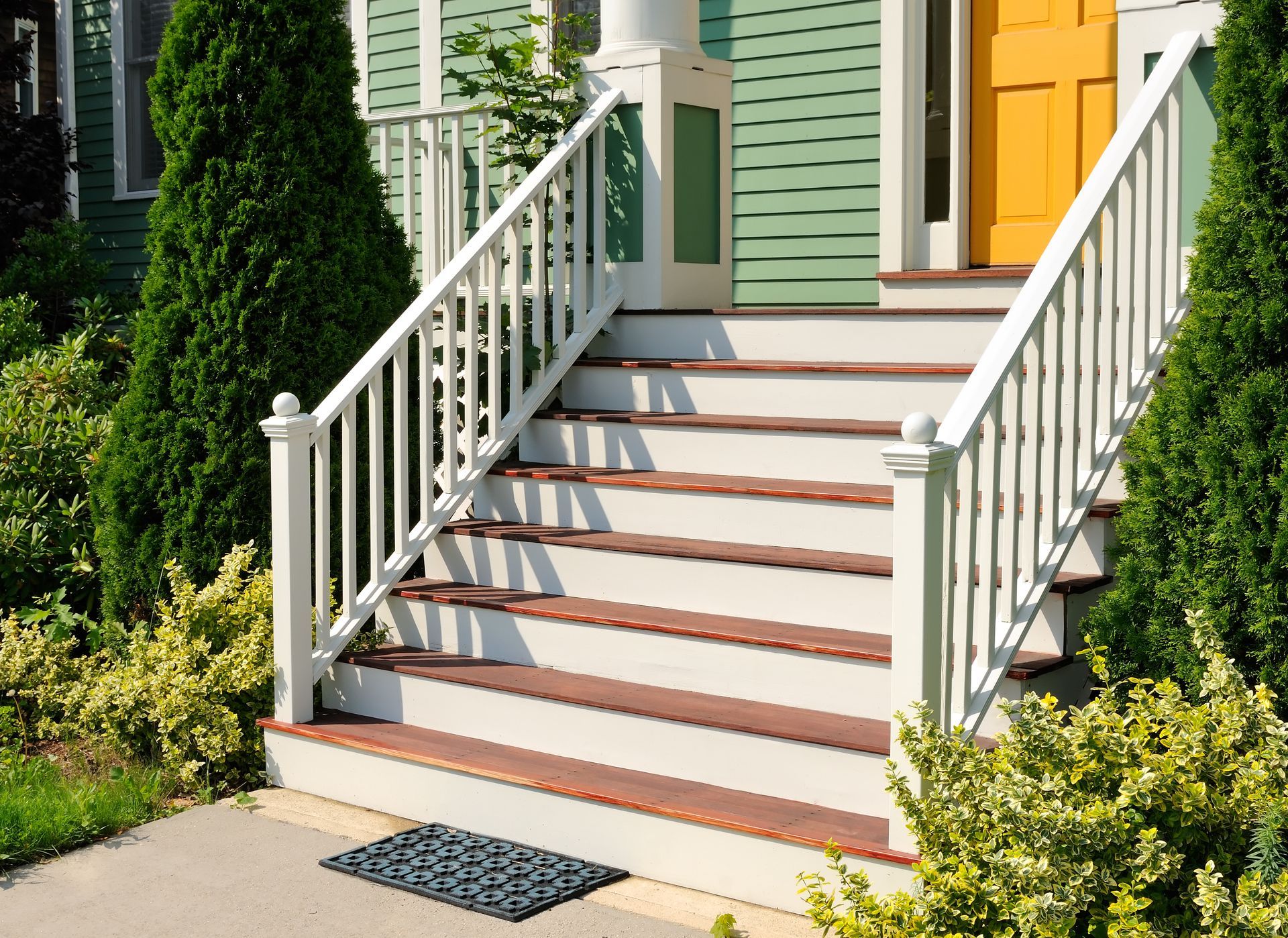 A green house with white stairs and a yellow door