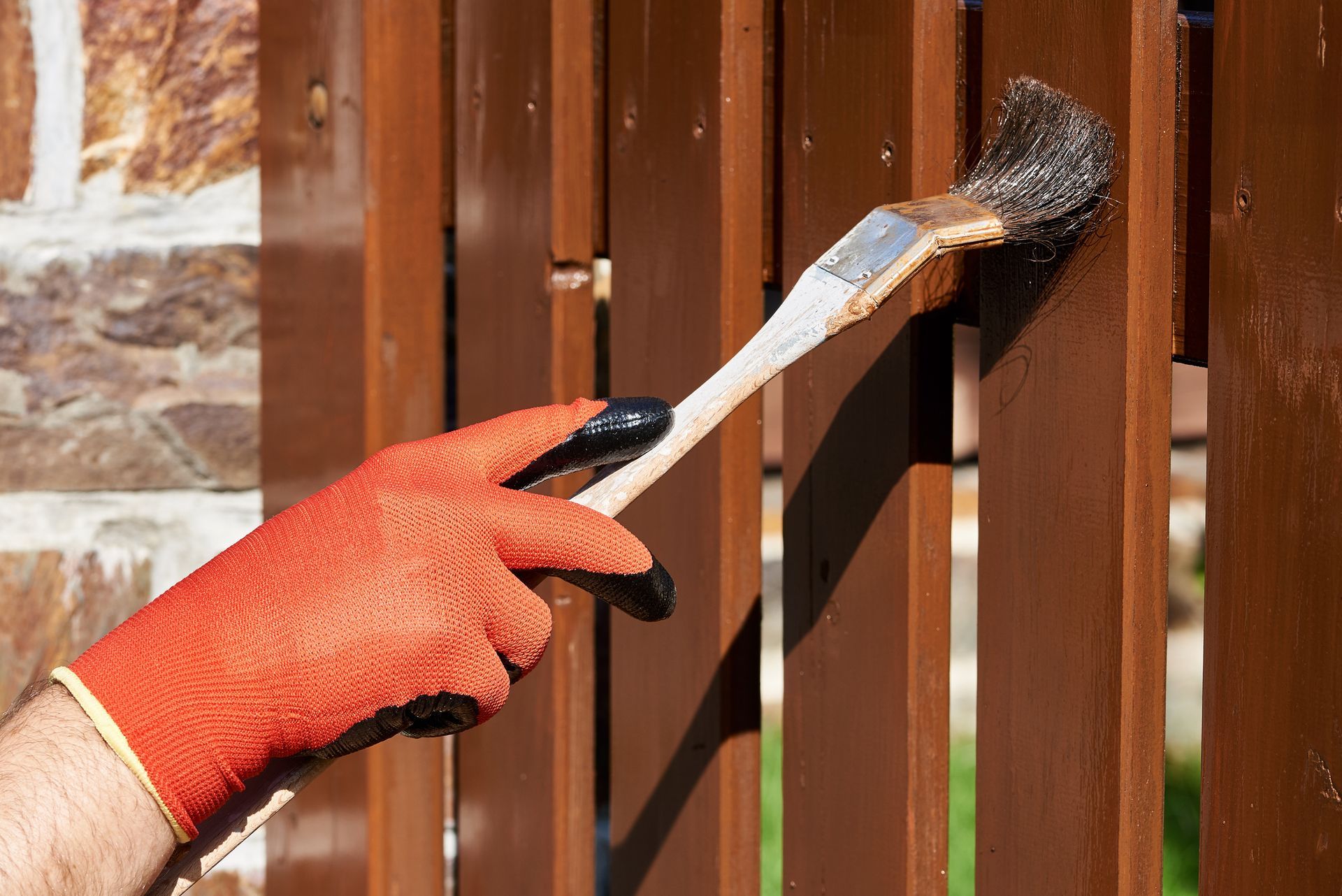 A person is painting a wooden fence with a brush.