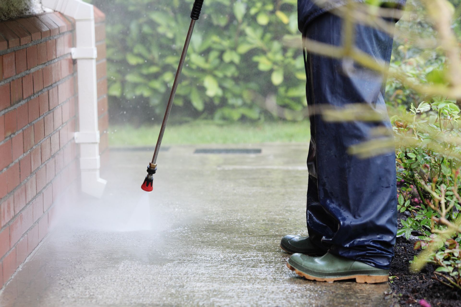 A person is using a high pressure washer to clean a sidewalk.