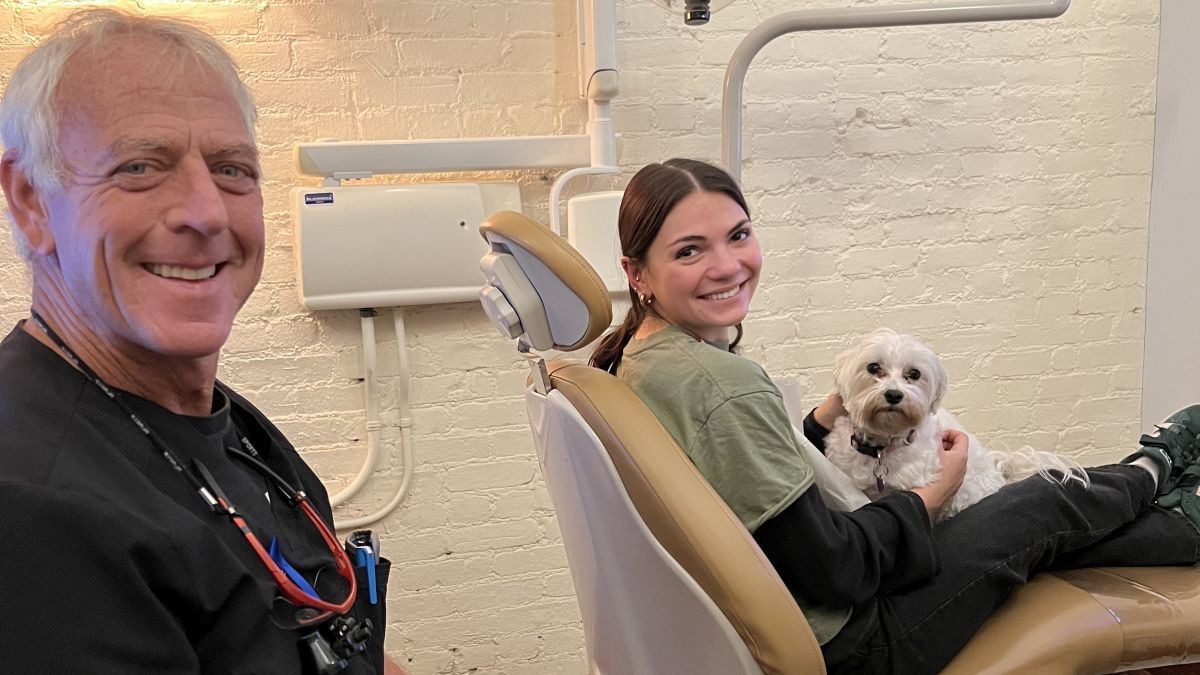Dr. Frederick Solomon and a dental patient with emotional support dog Oakley in her lap