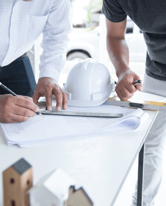 Two men are sitting at a table looking at a blueprint.